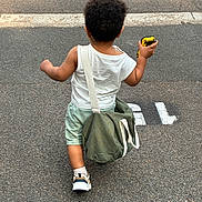 Tyler a rejoint le concours — aidez-le/la à gagner de superbes lots ! toddler, child, back_view, curly_hair, toy_car, green_bag, white_tank_top, mint_shorts, sneakers, walking, asphalt, street, sidewalk, outdoor, summer_clothing, casual, young_child, daytime, small_person, playful