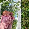 babies, infants, twins, children, portrait, pink_dresses, gingham, matching_outfits, outdoor, garden, greenery, vines, leaves, hedge, daylight, sitting, close_up, faces, curious, family_photo