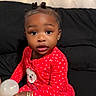 child, toddler, baby, portrait, sitting, bed, black_bedding, tufted_headboard, red_outfit, heart_pattern, pajamas, hair_buns, earrings, bracelets, toy, ball, indoors, bedroom, looking_at_camera, person
