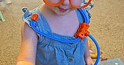 Luna joined the competition — help win amazing prizes! background, blue, carpet, child, cute, fun, furniture, glasses, hand, indoor, medical_toys, orange, plastic, play, pretend, room, stethoscope, syringe, toddler, toy