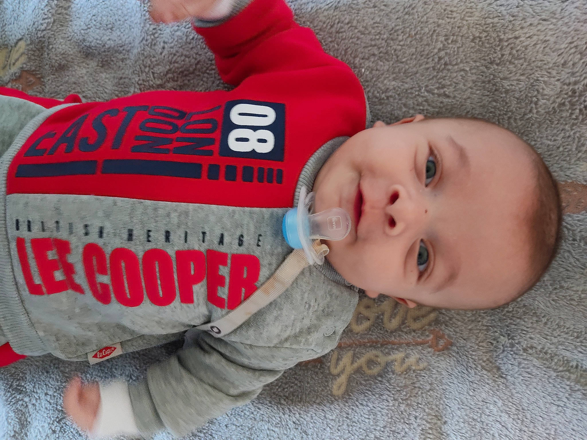 Kenzo participe au concours pour gagner de l'argent avec cette photo : baby, baby_toddler_clothing, cheek, child, comfort, flooring, font, grass, happy, nose, person, red, sitting, skin, sleeve, smile, t_shirt, toddler, tree, vacation