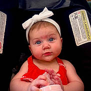 Isla joined the competition — help win amazing prizes! baby, infant, child, bottle, headband, red_dress, car_seat, warning_label, blue_eyes, hands, face, cute, indoors, person, sitting, feeding, closeup, expression, portrait, young