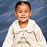 child, girl, portrait, smiling, happy, studio, indoor, tiara, hair_accessory, earrings, dress, cardigan, cream_clothing, formalwear, fashion, standing, front_facing, blue_background, professional_photography, princess