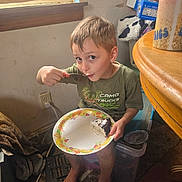 Brycen is registered to the contest to win money with this photo: child, boy, cake, plate, fork, sitting, barefoot, plastic_container, keyboard, window, blinds, table, cup, clothing, carpet, room, indoor, food, person, furniture