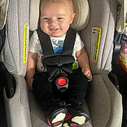 Paxton is registered to the contest to win money with this photo: baby, infant, child, smiling, car_seat, harness,  안전, portrait, indoors, seated, vehicle, canopy, padded_seat, colorful_shoes, black_clothing, happy, face, head, photograph, parenting