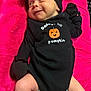 baby, infant, black_clothing, mittens, socks, headwrap, smile, pink_blanket, cute, lying_down, cheeky_expression, pumpkin_graphic, cozy, newborn, infant_fashion, portrait, child, human, soft_texture, indoors