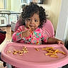 toddler, child, high_chair, food, french_fries, snack, curly_hair, pink, onesie, indoor, home, table, seat, eating, person, cute, baby, face, expression, furniture