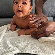 Jahleel a rejoint le concours — aidez-le/la à gagner de superbes lots ! baby, infant, hands, towel, couch, skin, person, child, smiling, curious, supporting, arm, fingers, adult, jewelry, ring, soft_texture, indoor, closeup, portrait