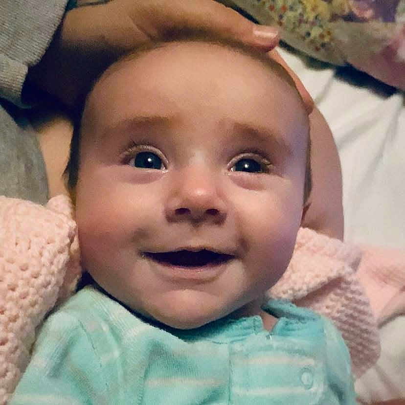 Abagail is registered to the contest to win money with this photo: baby, smiling, close_up, face, infant, blue_outfit, blanket, hand, skin, eyes, happy, child, soft, indoor, portrait, cute, newborn, person, head, cozy
