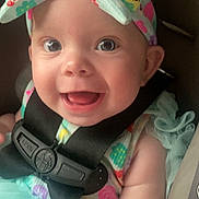 Delilah is registered to the contest to win money with this photo: baby, smiling, child, car_seat, seatbelt, headband, bow, colorful, happy, face, eyes, infant, clothing, tutu, sitting, cute, portrait, skin, cheerful, young