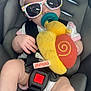 baby, car_seat, sunglasses, headband, pacifier, plush_toy, child, infant, seatbelt, reflection, person, hand, foot, clothing, toy, cute, indoor, seat, pink, yellow