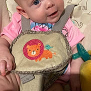 Delilah joined the competition — help win amazing prizes! animal_print, baby, bird, blue_eyes, child, closeup, cute, embroidery, face, hand, harness, indoors, infant, legs, lion, pacifier, pink_clothing, seat, smiling, toy