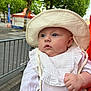 Lylia a rejoint le concours — aidez-le/la à gagner de superbes lots ! baby, child, curious, daylight, event, face, fence, hand, hat, headwear, infant, nature, outdoor, person, portrait, skin, street, tent, trees, white_clothing