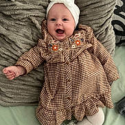 Lylia participe au concours pour gagner de l'argent avec cette photo : baby, child, smiling, headband, bow, dress, patterned_clothing, floral_embroidery, pillow, textured_pillow, socks, white_socks, frilly_socks, happy, infant, lying_down, indoor, cute, person, portrait