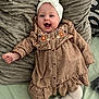 baby, child, smiling, headband, bow, dress, patterned_clothing, floral_embroidery, pillow, textured_pillow, socks, white_socks, frilly_socks, happy, infant, lying_down, indoor, cute, person, portrait