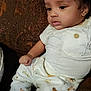 Isley is registered to the contest to win money with this photo: baby, child, curly_hair, white_shirt, patterned_pants, couch, brown_couch, indoor, seated, thoughtful, cute, infant, portrait, clothing, button, face, skin, sitting, young_child, home
