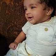 Isley joined the competition — help win amazing prizes! baby, child, infant, smiling, curly_hair, light_clothing, sitting, couch, patterned_fabric, indoors, cute, happy, portrait, one_person, closeup, small_child, young_child, button, comfortable, bright_eyes