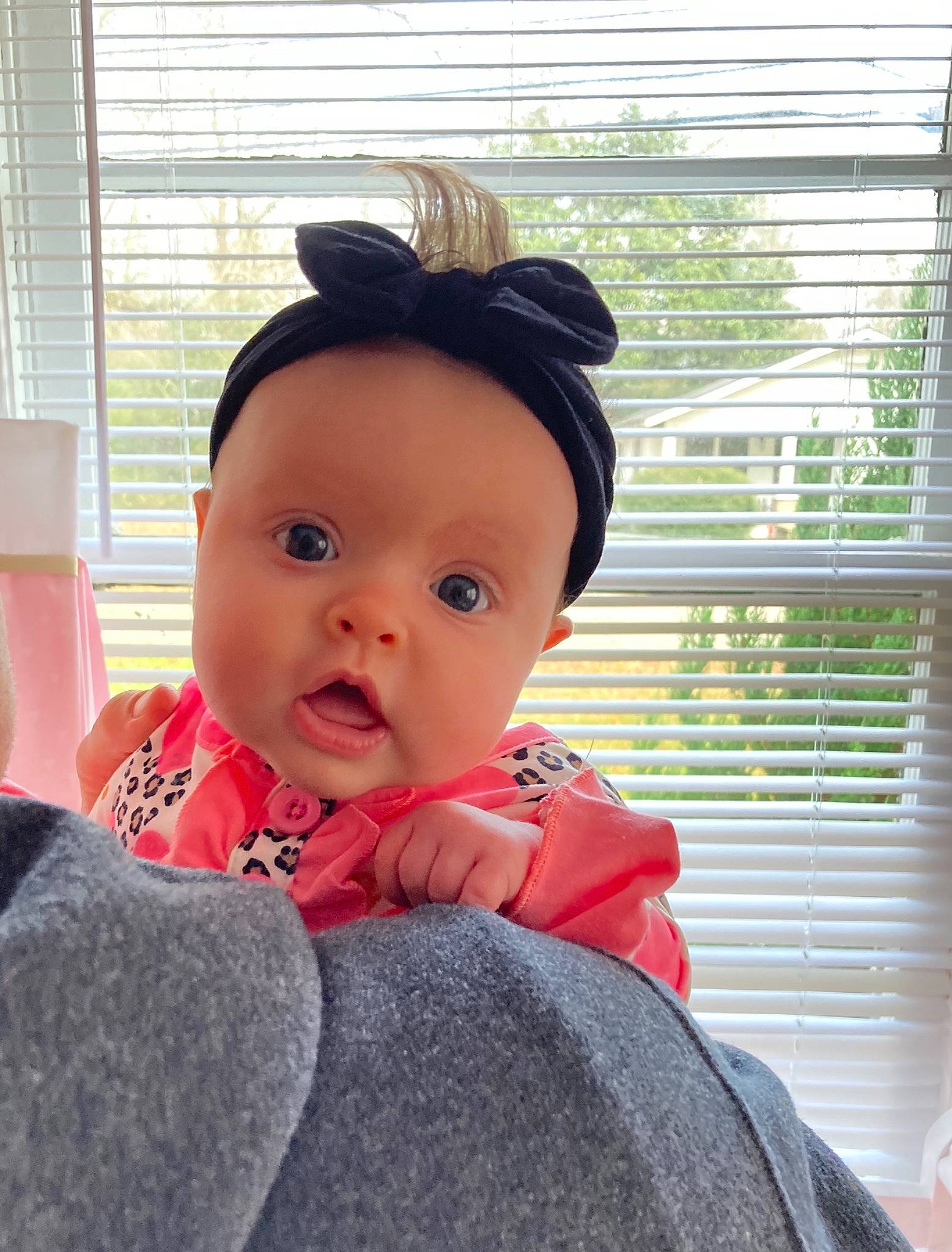 Hazel Grace is registered to the contest to win money with this photo: baby, baby_toddler_clothing, black_hair, cap, cheek, child, comfort, eyelash, fashion_accessory, happy, headgear, headwear, lip, person, sitting, sleeve, surprise, toddler, window, window_blind