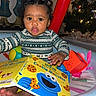 Mikayla is registered to the contest to win money with this photo: baby, child, toddler, indoor, book, cookie_monster, sesame_street, toy, play_area, christmas_tree, holiday, curly_hair, clothing, face, expression, reading, colorful, cute, infant, festive