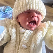 Sonny is registered to the contest to win money with this photo: baby, child, knit_hat, knit_sweater, white_clothing, yawning, crying, closeup, indoor, person, infant, cute, soft_texture, warm_clothing, small_face, newborn, portrait, human, expression, cozy