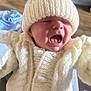 baby, child, knit_hat, knit_sweater, white_clothing, yawning, crying, closeup, indoor, person, infant, cute, soft_texture, warm_clothing, small_face, newborn, portrait, human, expression, cozy