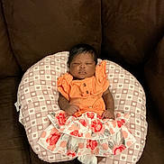 Kehlani is registered to the contest to win money with this photo: baby, infant, sleeping, couch, pillow, orange_clothing, floral_skirt, patterned_pillow, indoor, cozy, child, young_child, resting, cute, small_hands, white_socks, brown_hair, peaceful, portrait, soft_lighting