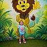 Auralia joined the competition — help win amazing prizes! child, toddler, smiling, standing, lion_mural, cartoon, jungle, greenery, grass, shorts, tshirt, shoes, panda, colorful, wall_art, happy, indoor, playful, person, background