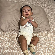 Emiliano is registered to the contest to win money with this photo: baby, infant, child, smiling, portrait, lying_down, bed, pillow, bedding, patterned_fabric, onesie, socks, bracelet, indoor, home, cute, happy, relaxed, front_view, photography