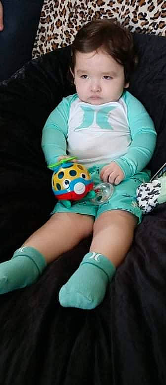 Milo is registered to the contest to win money with this photo: arm, baby, baby_toddler_clothing, clothing, comfort, finger, hand, human_leg, joint, knee, leg, pattern, person, personal_protective_equipment, pink, sitting, sleeve, sock, stuffed_toy, thigh