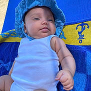 Nyah a rejoint le concours — aidez-le/la à gagner de superbes lots ! baby, infant, blue_hat, white_onesie, towel, blue_towel, yellow_towel, outdoor, sunlight, skin, arm, face, hand, relaxing, summer, child, portrait, cute, chubby, laying_down