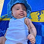 baby, infant, blue_hat, white_onesie, towel, blue_towel, yellow_towel, outdoor, sunlight, skin, arm, face, hand, relaxing, summer, child, portrait, cute, chubby, laying_down