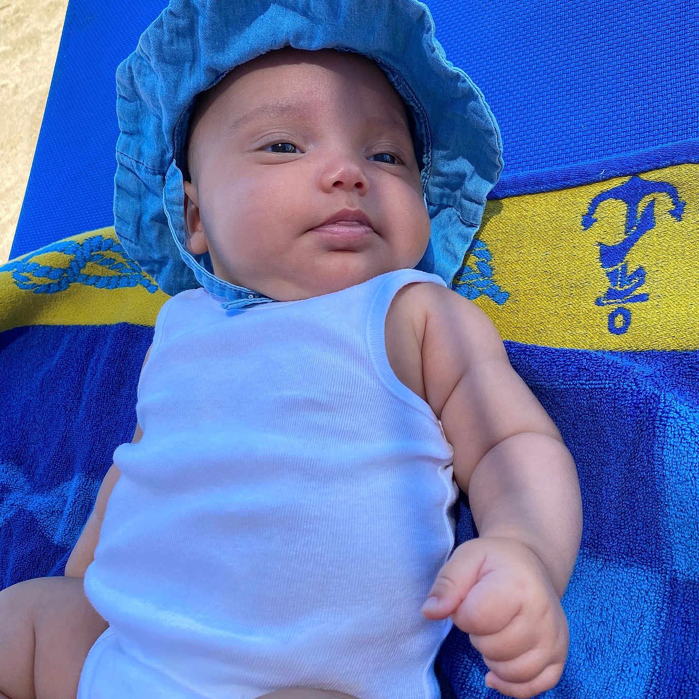 Nyah a rejoint le concours — aidez-le/la à gagner de superbes lots ! arm, baby, blue_hat, blue_towel, child, chubby, cute, face, hand, infant, laying_down, outdoor, portrait, relaxing, skin, summer, sunlight, towel, white_onesie, yellow_towel