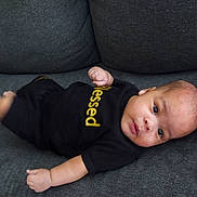 Hezekiah joined the competition — help win amazing prizes! baby, infant, child, couch, sofa, clothing, black_shirt, text, blessed, face, eyes, arms, legs, skin, indoors, furniture, person, lying_down, expression, cute