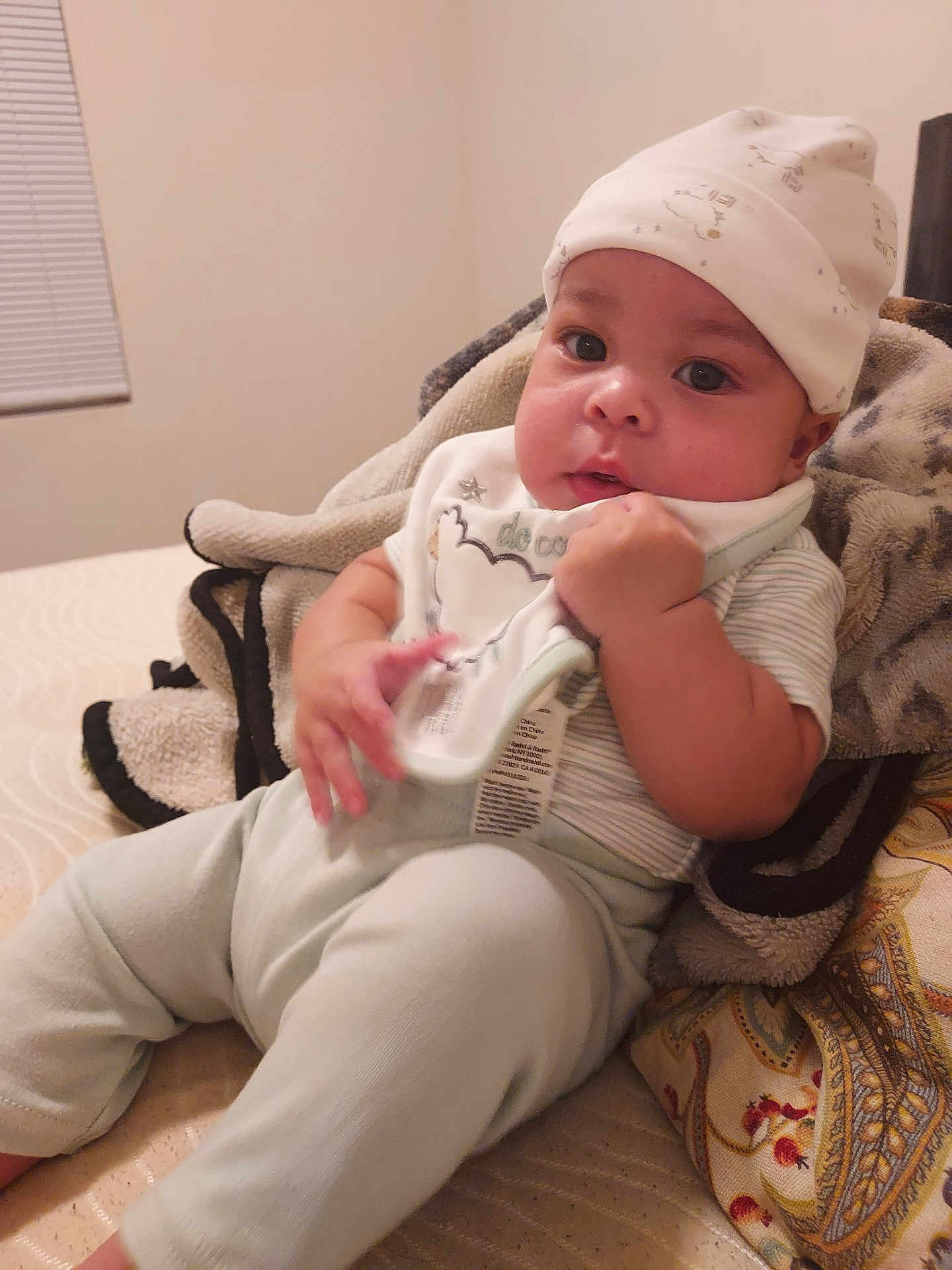 Hezekiah is registered to the contest to win money with this photo: baby, infant, hat, clothing, blanket, bed, pillow, face, hand, sitting, indoors, cute, child, young, soft, cozy, portrait, expression, warm, comfortable