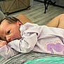 baby, infant, purple_onesie, seahorse_patch, striped_clothing, person, lap, hand, face, indoor, flooring, wooden_floor, couch, gray_fabric, skin, newborn, curious, closeup, baby_clothes, relaxed
