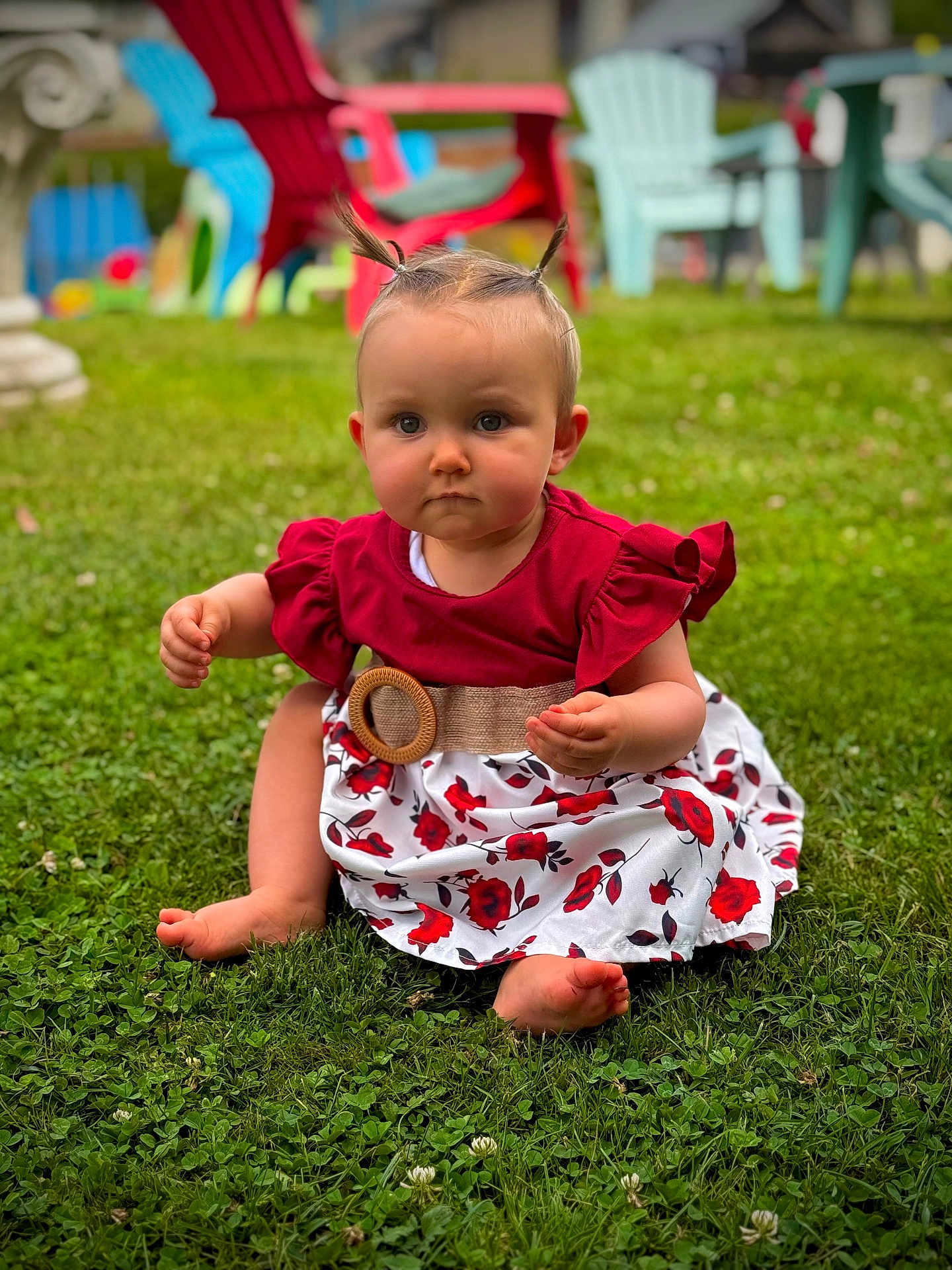 Melina participe au concours pour gagner de l'argent avec cette photo : baby, child, grass, outdoor, dress, red_top, floral_pattern, belt, ponytails, barefoot, greenery, summer, sitting, lawn_chair, blurred_background, cute, serious_expression, nature, playtime, portrait
