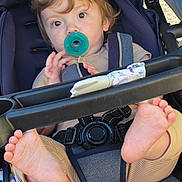 Winston is registered to the contest to win money with this photo: toddler, child, stroller, pacifier, barefeet, curly_hair, seatbelt, casual_clothing, outdoor, baby, infant, cute, playful, portrait, young_child, relaxed, daylight, seat, child_safety, expression