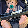 toddler, child, stroller, pacifier, barefeet, curly_hair, seatbelt, casual_clothing, outdoor, baby, infant, cute, playful, portrait, young_child, relaxed, daylight, seat, child_safety, expression