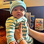 Theo joined the competition — help win amazing prizes! baby, child, person, striped_clothing, blue_hat, hat_with_ears, hand, watch, wooden_table, indoor, menu, framed_picture, window, light, face, cute, infant, seated, holding, casual