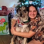 woman, dog, christmas_tree, gift, holiday, smile, indoor, floor, wrapped_presents, decorations, festive, happy, hug, canine, pet, casual_clothing, tile_floor, scarf, friendship, celebration