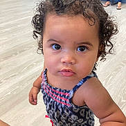 Nevaeh is registered to the contest to win money with this photo: toddler, child, curly_hair, indoor, floor, person, blue_outfit, patterned_clothing, barefoot, looking_up, cute, skin, face, eyes, expression, standing, casual, people, home, furniture