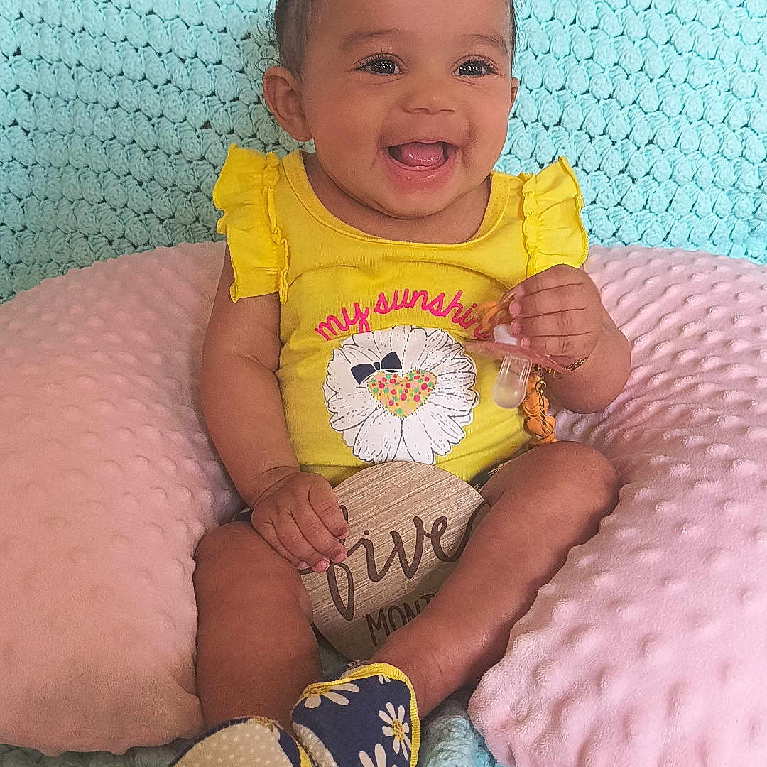 Ka'Hari joined the competition — help win amazing prizes! baby, blanket, child, cozy, cushion, cute, decor, footwear, hair_bows, happy, home, indoor, infant, pacifier, person, portrait, seated, smiling, wooden_sign, yellow_clothing