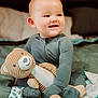 baby, child, plush_toy, teddy_bear, bed, blanket, pajamas, smiling, happy, indoors, soft_toy, cute, comfort, cozy, person, young_child, seated, portrait, sleepwear, warm_lighting