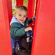 Antonin a rejoint le concours — aidez-le/la à gagner de superbes lots ! toddler, child, playground, red, steering_wheel, outdoor, park, greenery, jacket, hoodie, jeans, sneakers, smile, happy, person, toy, play, daylight, cute, fun