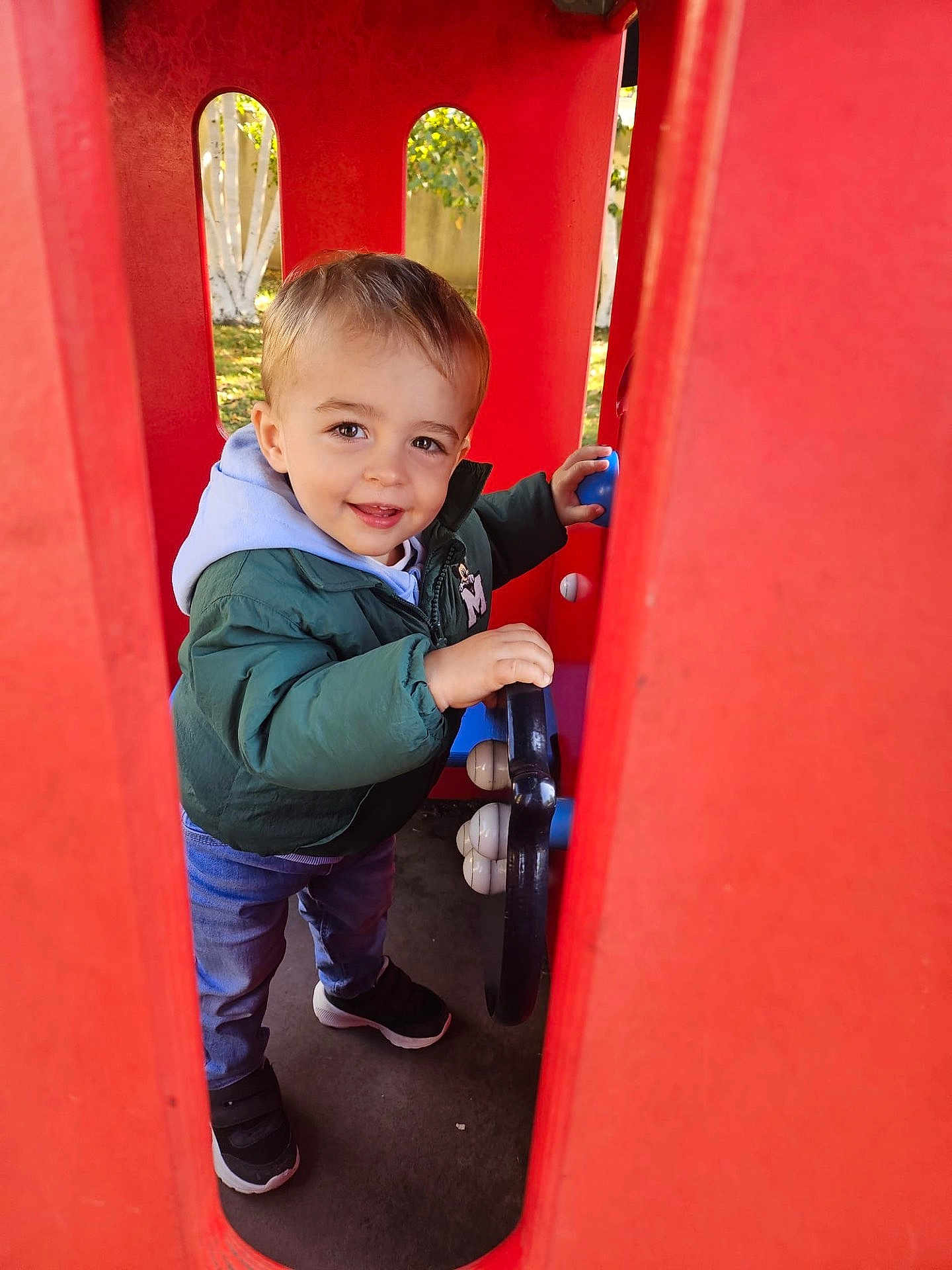 Antonin a rejoint le concours — aidez-le/la à gagner de superbes lots ! toddler, child, playground, red, steering_wheel, outdoor, park, greenery, jacket, hoodie, jeans, sneakers, smile, happy, person, toy, play, daylight, cute, fun