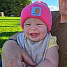 baby, infant, child, smiling, happy, portrait, pink_hat, beanie, carhartt, outdoor, park, grass, trees, blue_sky, sunlight, adult, parent, cuddling, bib, family