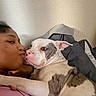 person, dog, face, hug, affection, indoor, close_up, pet, cuddle, wall, texture, expression, brown_skin, white_dog, patches, resting, relaxed, love, bond, companion