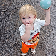 Laiken is registered to the contest to win money with this photo: toddler, child, ball, toy, outdoor, gravel, play, clothing, shorts, shirt, shoes, blonde_hair, person, young_child, curious, casual, standing, hand, fingers, portrait