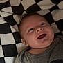 baby, infant, smiling, checkered_blanket, onesie, clothing, face, happy, closeup, portrait, lying_down, newborn, cheek, mouth_open, eyes, ear, head, indoor, diaper_brand_huggies, soft_fabric