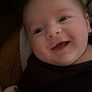 Kylo is registered to the contest to win money with this photo: baby, infant, smiling, face, eyes, blanket, onesie, cheek, mouth, portrait, close_up, cute, happy, indoors, towel, bedding, arm, newborn, cozy, soft_lighting